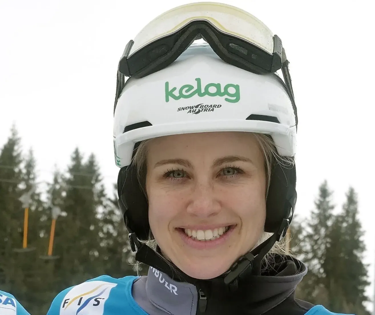 Eine lächelnde Frau mit einem weißen Helm, auf dem das Wort 'kelag' steht, und einer blau-schwarzen Jacke mit FIS auf der linken Seite.