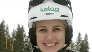 Eine lächelnde Frau mit einem weißen Helm, auf dem das Wort 'kelag' steht, und einer blau-schwarzen Jacke mit FIS auf der linken Seite.