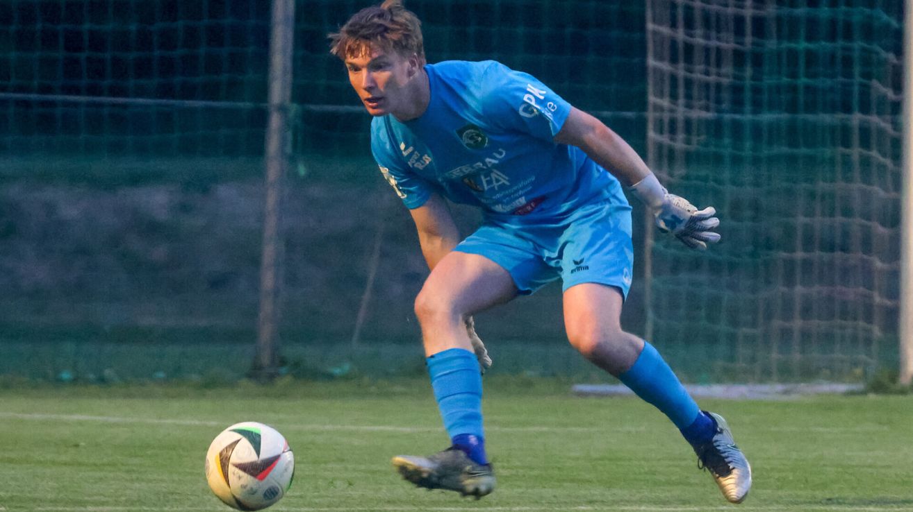 Ein Fußballspieler in blauer Uniform läuft auf einem Rasenfeld auf den Ball zu.