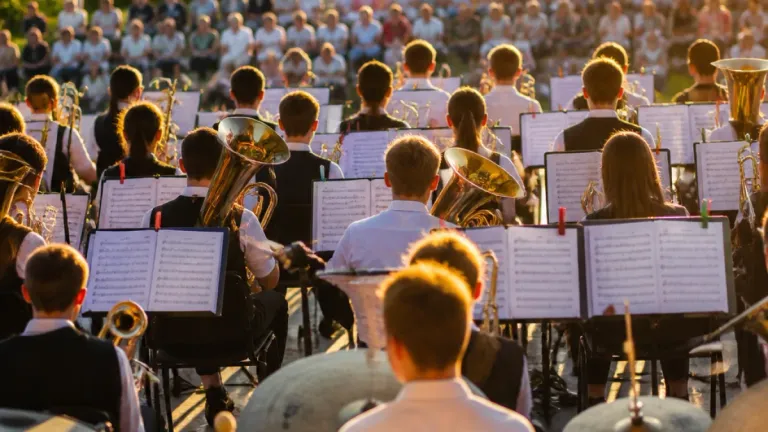 Eine Schulband spielt auf der Bühne mit Blech- und Perkussionsinstrumenten, mit einem großen Publikum im Hintergrund.