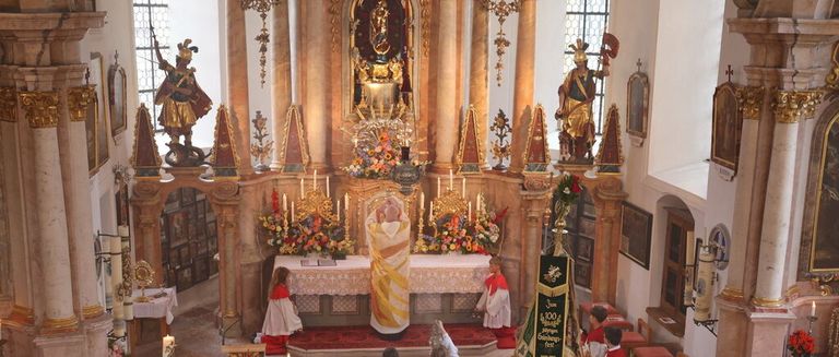 Ein Priester führt eine Zeremonie an einem Altar in einer Kirche mit goldenen Statuen und Blumen durch.