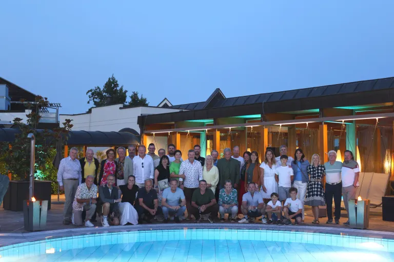 Eine Gruppe von Menschen posiert für ein Foto vor einem Gebäude mit Pool in der Dämmerung.