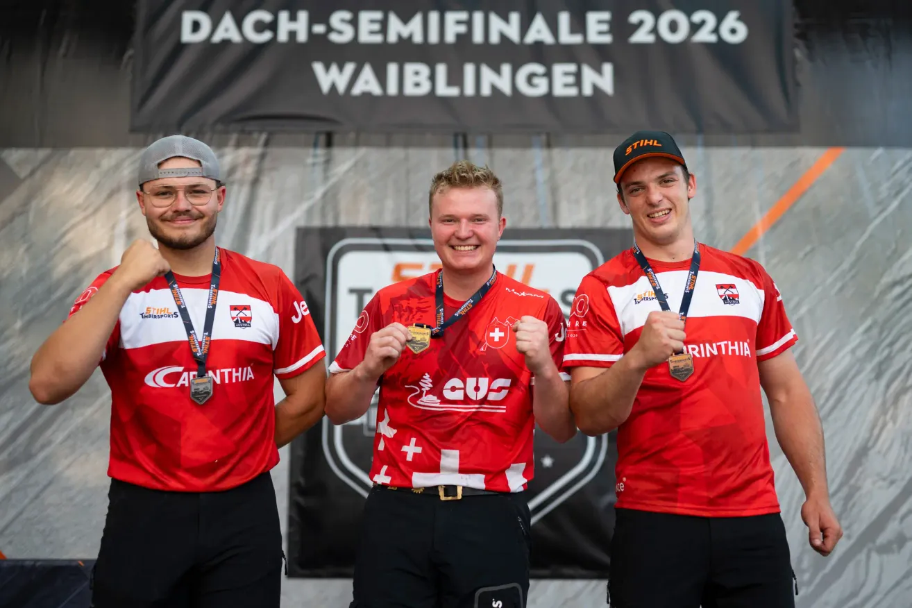 Drei Männer in roten Trikots mit Medaillen um den Hals stehen gemeinsam auf einer Bühne. Der Mann in der Mitte trägt einen schwarzen Hut mit dem Wort 'Stihl' darauf. Der Banner hinter ihnen lautet 'DACH-SEMIFINALE 2026 WAIBLINGEN'.