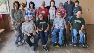 Eine Gruppe von Menschen, einige in Rollstühlen, lächeln und posieren für ein Foto in einem Raum mit Holzwänden und einem Banner.
