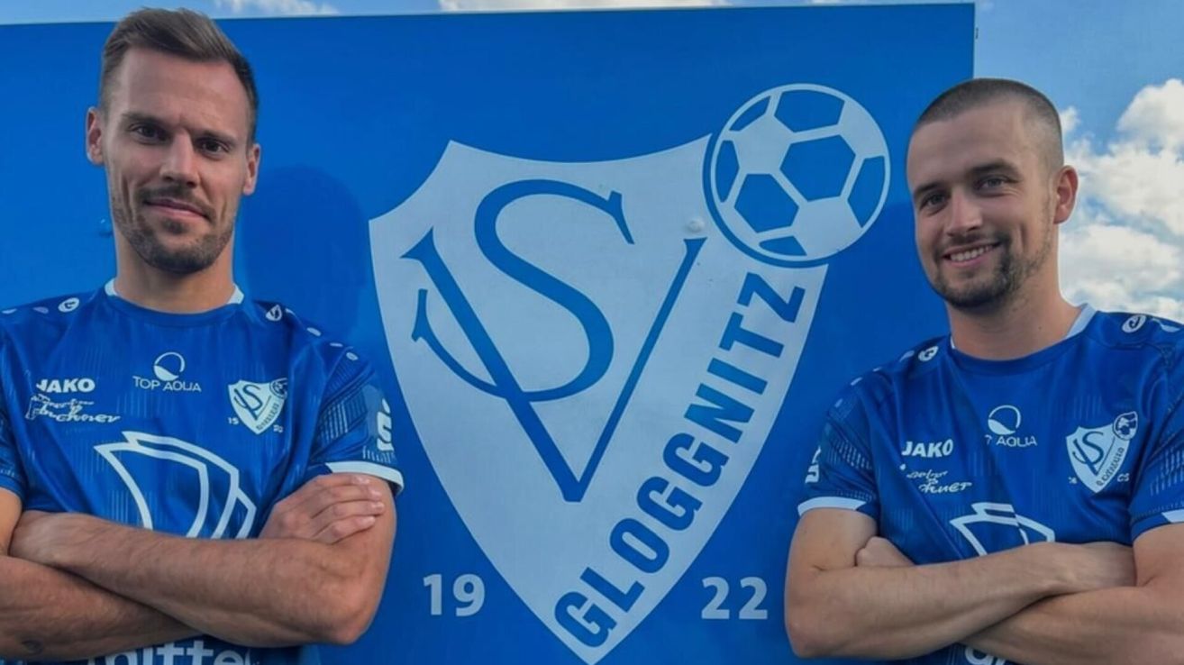 Zwei Männer in blauen Trikots stehen neben einem blauen Banner mit einem Fußballlogo und dem Text 'GLOGGNITZ' und den Zahlen '19' und '22'.
