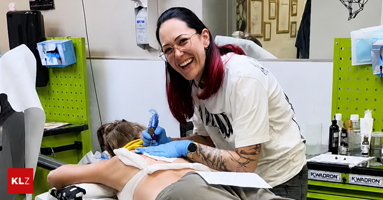 Eine Frau mit roten Haaren und Brille lächelt, während sie das Rücken eines Kindes in einem Studio tätowiert.