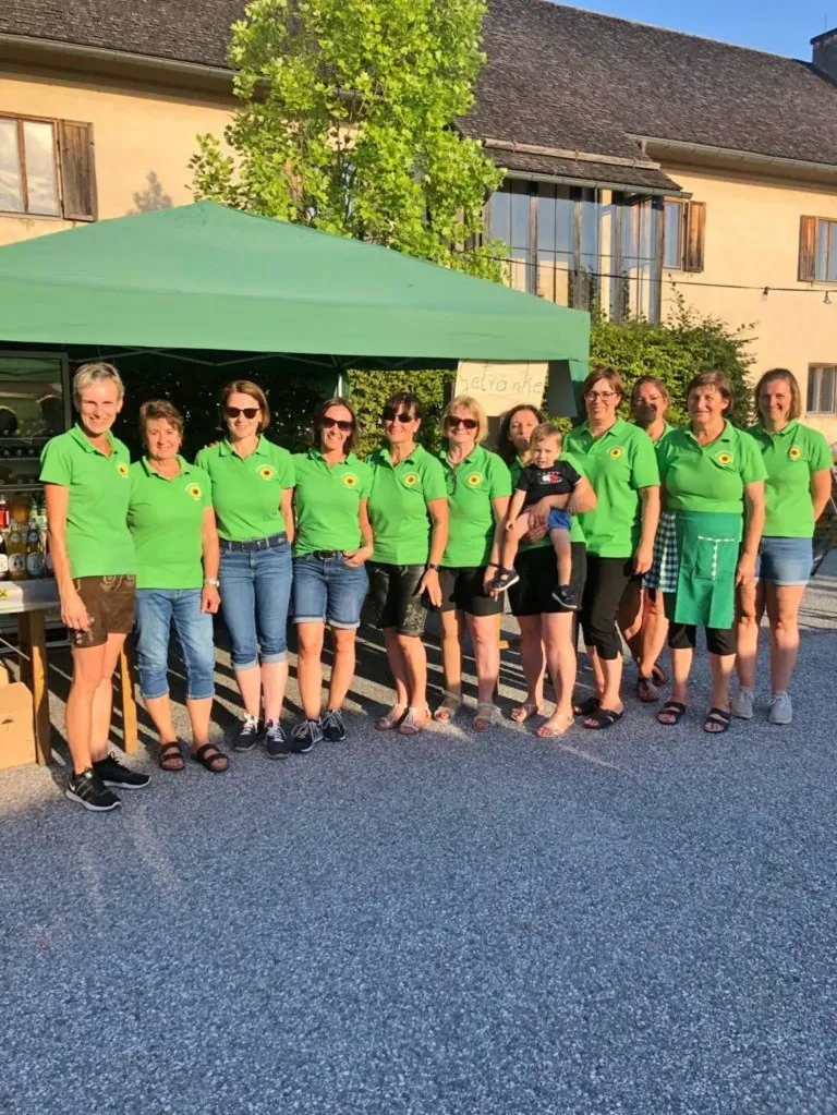 Eine Gruppe von Frauen in grünen Shirts und Shorts steht zusammen unter einem grünen Zelt, wobei eine Frau ein Baby hält.