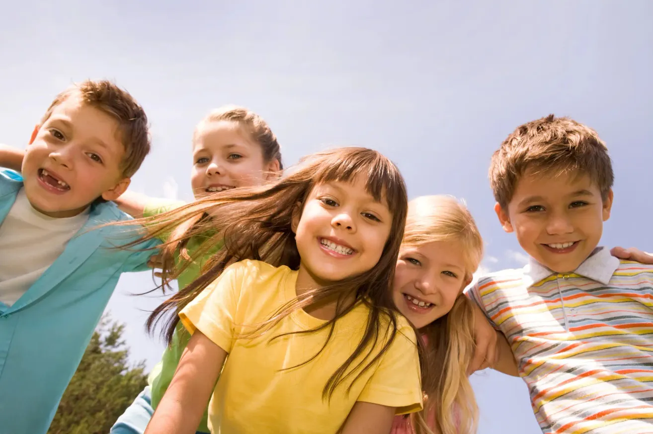 Eine Gruppe von Kindern, die lächeln und unter einem klaren blauen Himmel eng beieinanderstehen.