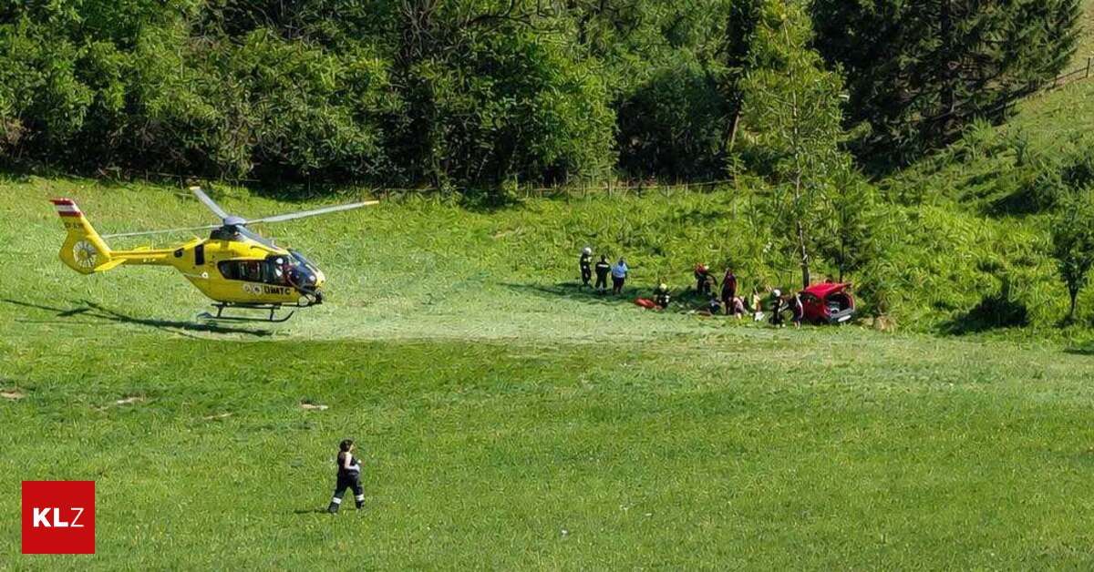 Ein Hubschrauber landet auf einem Grasfeld, umzingelt von Menschen, die eine rote Karre zu retten scheinen. Einige tragen Helme.