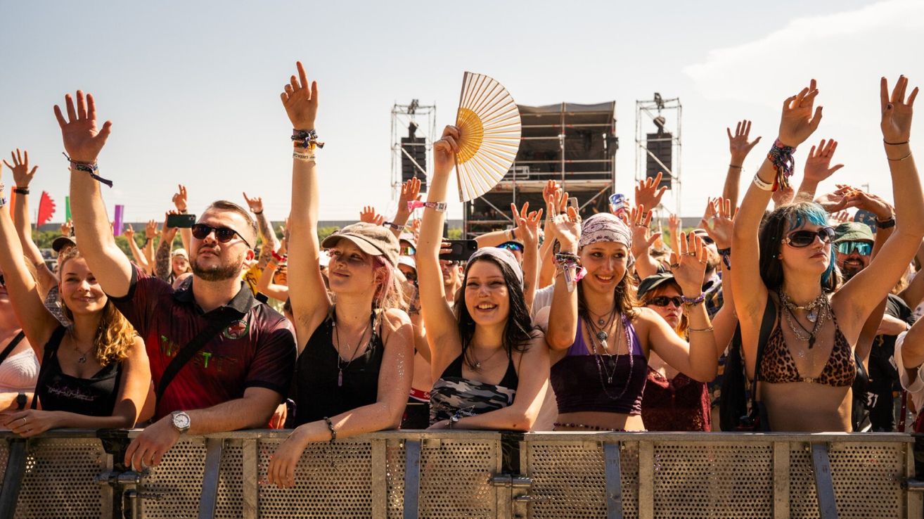 Eine Gruppe von Menschen auf einem Musikfestival, die ihre Hände heben und lächeln, mit einer Frau, die in der Mitte einen Fächer hält.