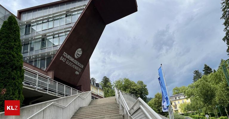 Der Eingang der Tourismusschule in Bad Gleichenberg, Österreich, zeigt ein modernes architektonisches Design mit einem großen Schild und Treppen, die zum Gebäude führen. Eine blaue Flagge ist auf der rechten Seite sichtbar.