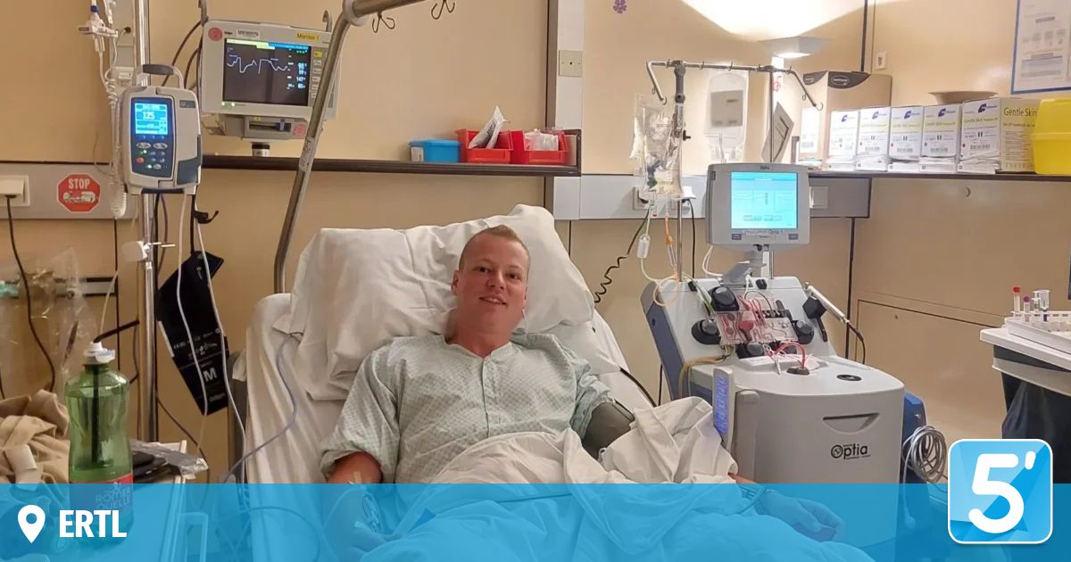 Ein Mann im Krankenhausbett mit medizinischer Ausrüstung um ihn herum, lächelt in die Kamera.