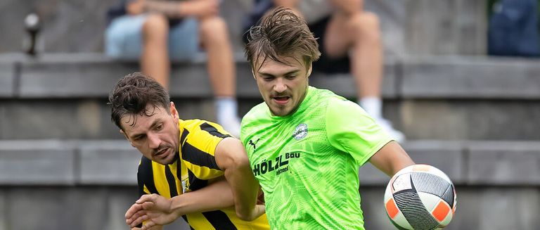 Zwei Fußballspieler kämpfen um den Ball. Einer in einem grünen Trikot hält den Ball, während der andere in einem gelben und schwarzen Trikot versucht, ihn zu stehlen.