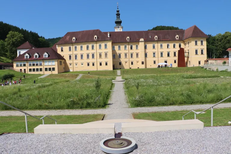 A large yellow building with a brown roof and a tower, surrounded by a grassy field and a walkway leading to it.