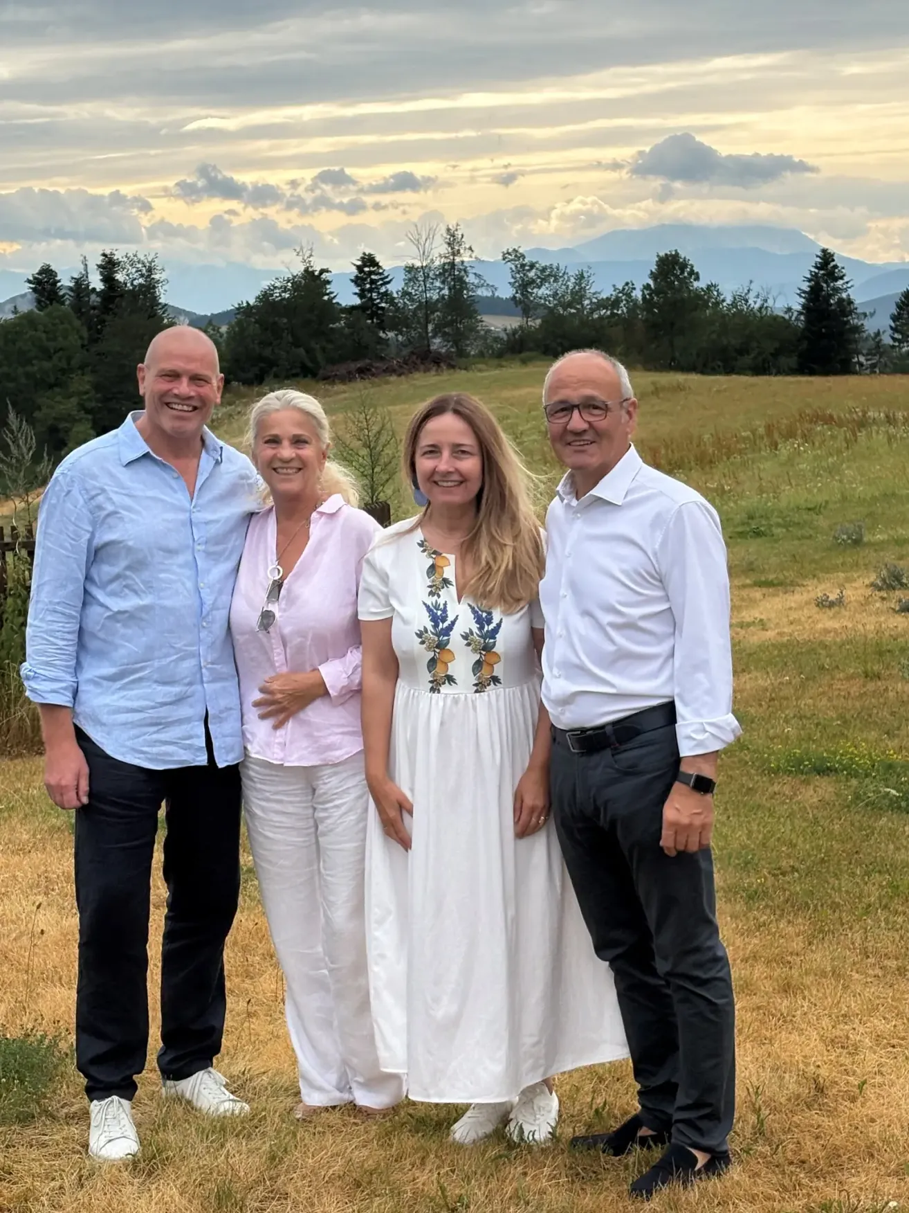 Vier Personen stehen in einem Feld mit einer Bergkette im Hintergrund. Zwei Frauen und zwei Männer, alle lächeln.