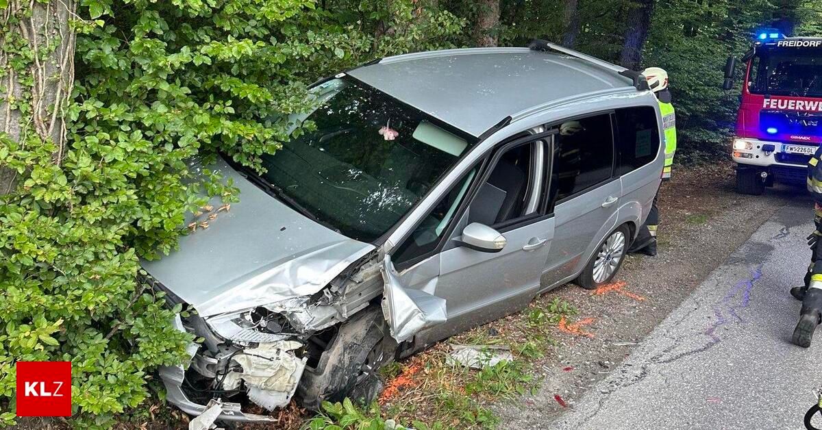 Ein silberner Minivan ist an der Straßenseite schwer beschädigt, mit erheblichen Schäden an der Front. Eine Person in einer gelben Weste steht in der Nähe.