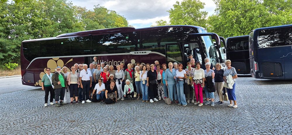 Eine Gruppe von Menschen, wahrscheinlich Touristen, posiert für ein Foto vor einem großen, dunklen Bus mit dem Wort 'Heiland' darauf.