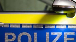 Eine Nahaufnahme der Seite eines Polizeiwagens mit dem Wort 'POLIZEI' in reflektierenden silbernen Buchstaben auf blauem Hintergrund.
