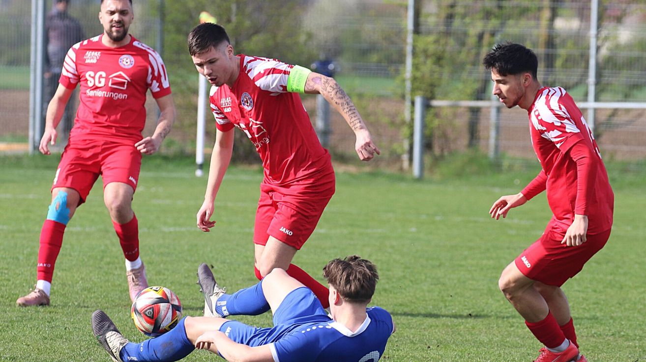 Ein Fußballspieler in roter Uniform fällt zu Boden, während ein anderer Spieler in Blau auf dem Gras liegt.
