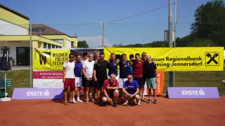 Eine Gruppe von Männern in Freizeitkleidung und mit Sonnenbrillen posiert für ein Foto auf einem Tennisplatz mit Bannern im Hintergrund.