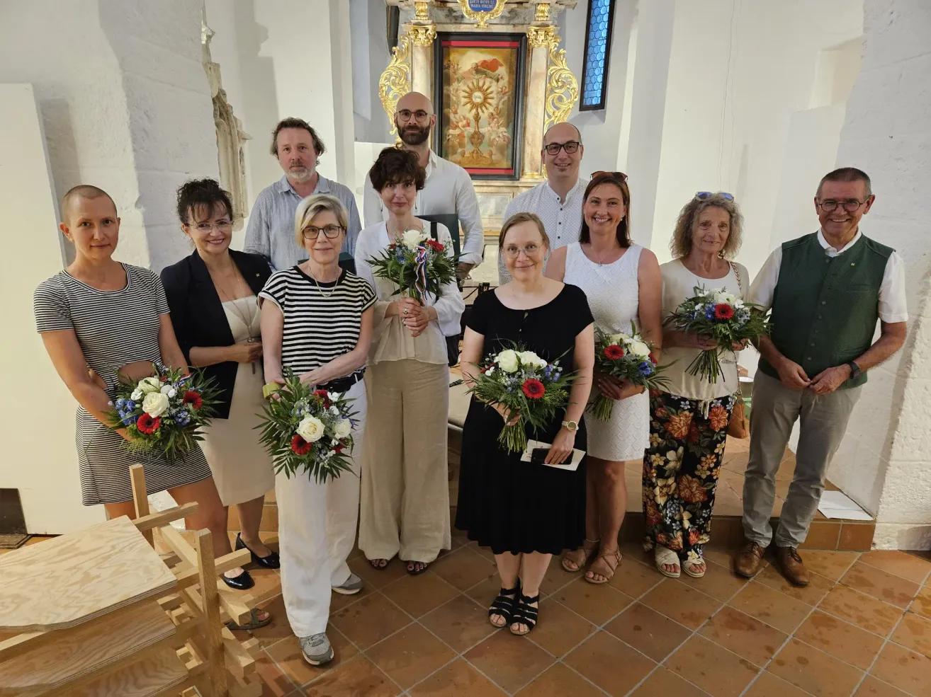Eine Gruppe von Menschen in einer Kirche, die Blumensträuße halten, lächeln und für ein Foto posieren.