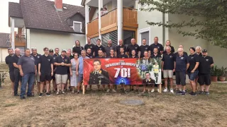 Eine Gruppe von Menschen in Uniform und Freizeitkleidung posiert für ein Foto vor einem Haus mit einem Banner, das 70 Jahre Dienst feiert.