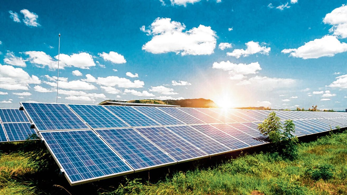 A large array of solar panels is installed on a grassy field under a bright blue sky with scattered clouds.
