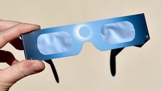 Eine Person hält ein Paar blaue Sonnenfinsternis-Brillen mit klaren Gläsern und einem blauen Rahmen.