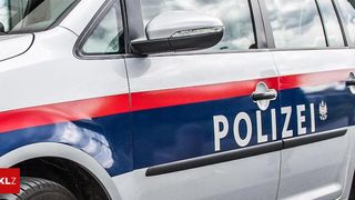 Ein Nahaufnahme von der Seite eines Polizeiwagens mit roten und blauen Streifen und dem Wort 'POLIZEI' in weiß. Der Seitenspiegel des Autos ist silber.