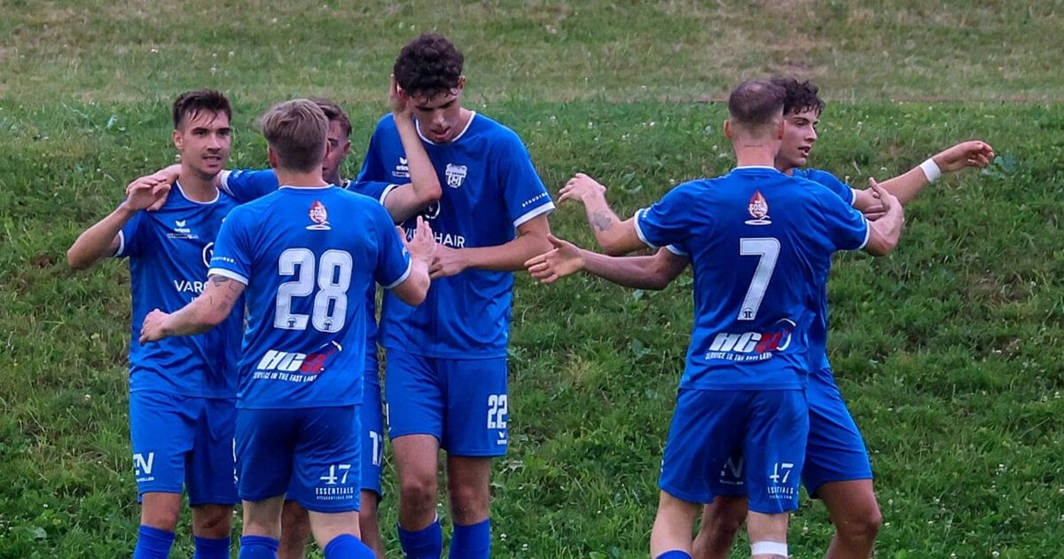Eine Gruppe junger Fußballer in blauen Trikots feiert ein Tor auf einem Rasenfeld.