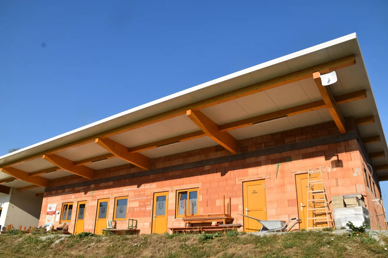 A new building under construction with orange doors and wooden supports, a wheelbarrow and ladders nearby.