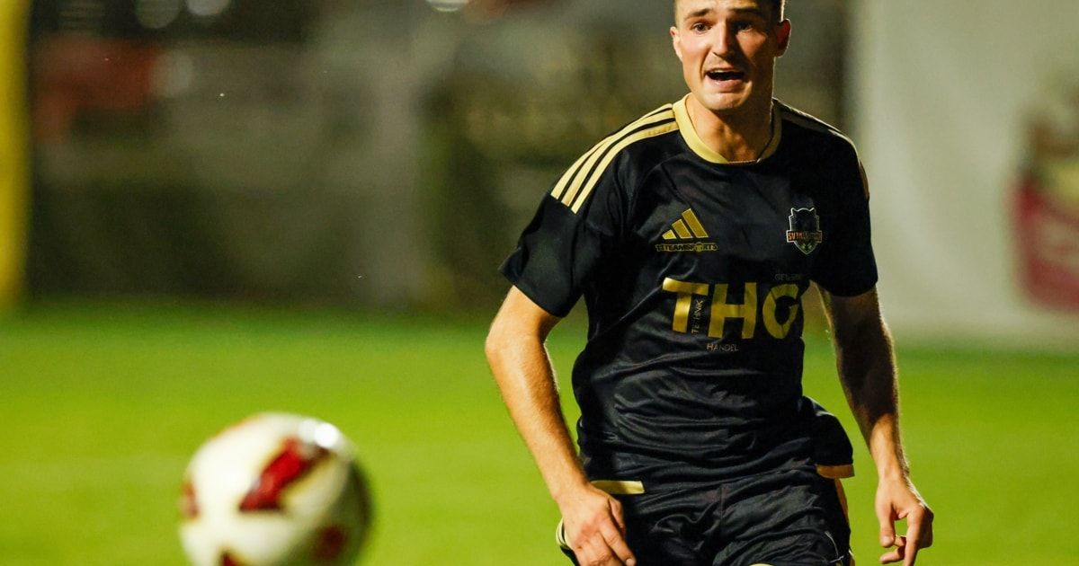 Ein Fußballspieler in einem schwarzen und gelben Trikot mit 'THG' auf der Vorderseite läuft auf einem Feld.