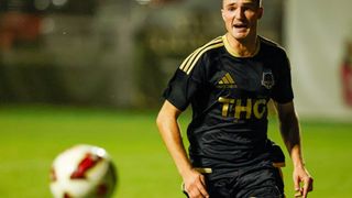 Ein Fußballspieler in einem schwarzen und gelben Trikot mit 'THG' auf der Vorderseite läuft auf einem Feld.