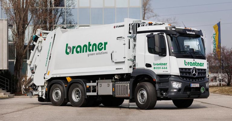 Ein weißer brantner Müllwagen mit grünen Akzenten vor einem Gebäude geparkt. Der Lkw hat den Text brantner green solutions an der Seite.
