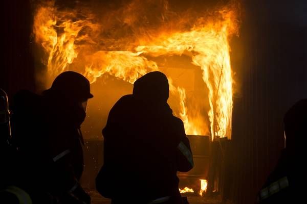 Feuerwehrleute in Schutzkleidung stehen vor einem brennenden Gebäude und beobachten die intensiven Flammen.
