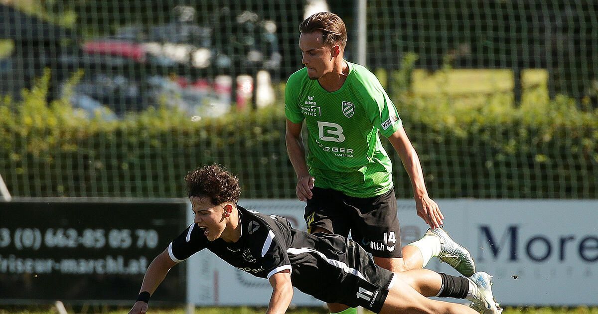 Zwei Fußballspieler in Aktion, einer in Grün und der andere in Schwarz, sind auf einem Feld in einem dynamischen Spiel engagiert. Der Spieler in Grün steht, während der Spieler in Schwarz zum Boden taucht.
