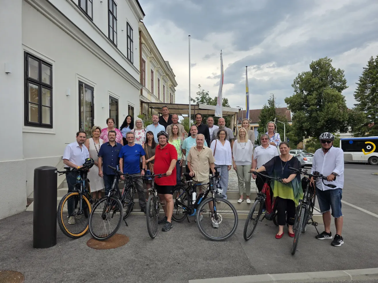 A group of people are posing for a photo with their bicycles in front of a building.