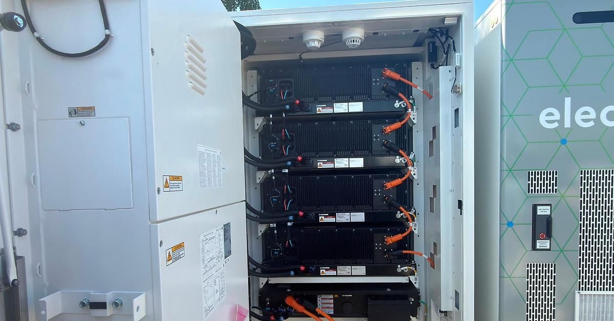 An open electrical enclosure with multiple battery packs and wires connected, with two surveillance cameras mounted on top.