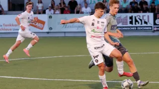 Two soccer players are competing on a field, one in a white jersey with the number 11, and the other in a gray jersey. They are both running towards the ball.