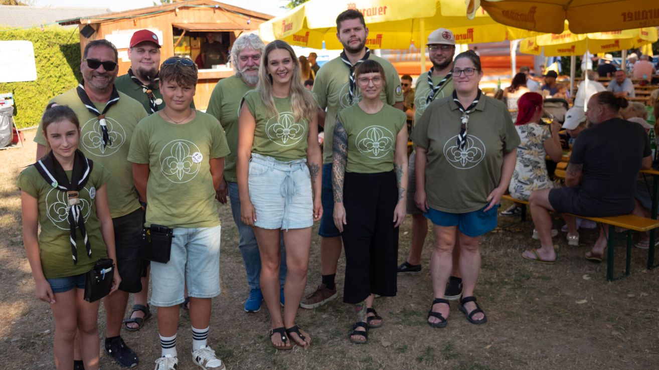 Eine Gruppe von Menschen in grünen T-Shirts mit einem weißen Logo posiert für ein Foto bei einer Outdoor-Veranstaltung.