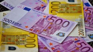 Ein Haufen Euro-Banknoten, einschließlich einer 500-Euro-Note, ist auf einem gelben Hintergrund angeordnet. Die 500-Euro-Note zeigt ein Gebäude und Sterne, während andere Noten verschiedene Designs aufweisen.