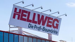 Ein großes Schild für Hellweg, einen professionellen Baumarkt, mit roten und weißen Farben und einem klaren blauen Himmel im Hintergrund.