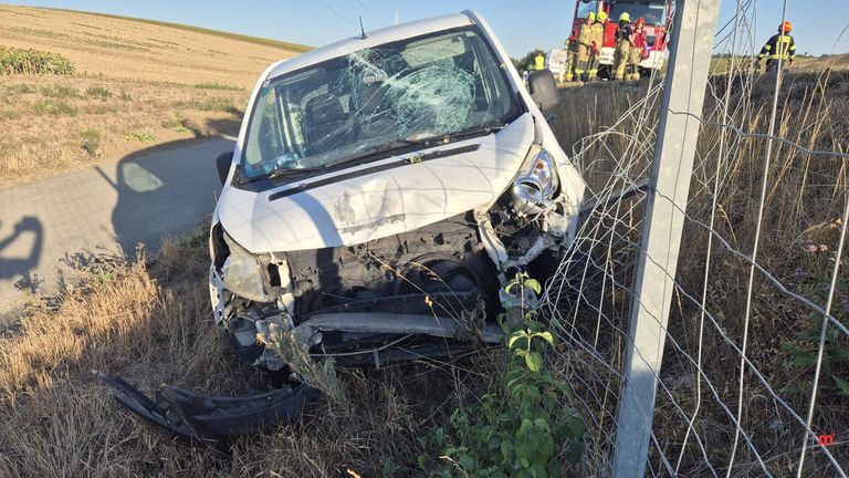 Ein weißer Lieferwagen mit zertrümmerter Front steht am Straßenrand, mit Rettungskräften in der Nähe.