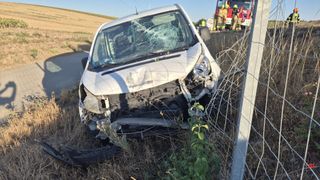 Ein weißer Lieferwagen mit zertrümmerter Front steht am Straßenrand, mit Rettungskräften in der Nähe.