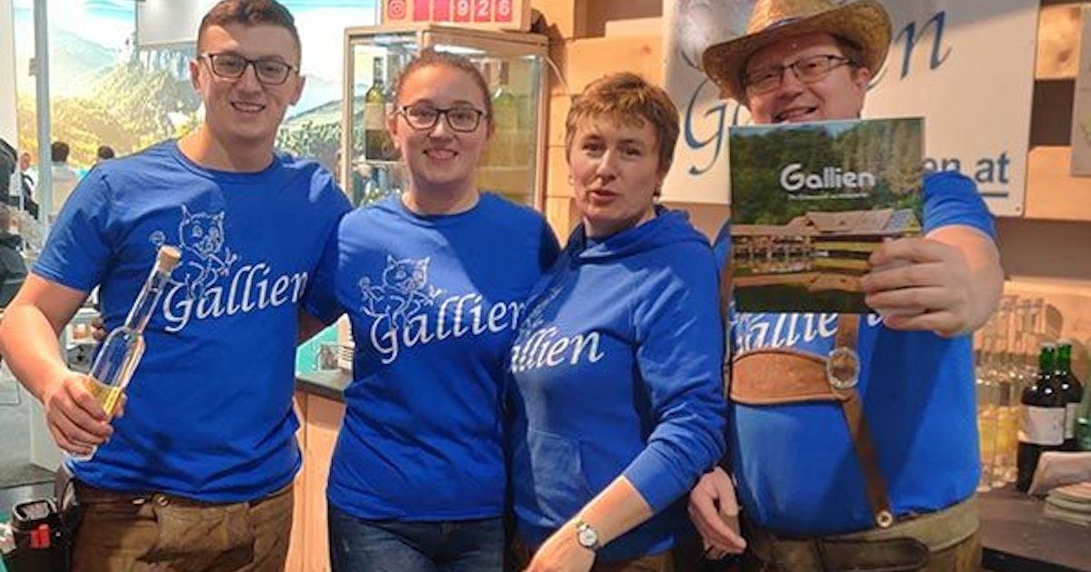 Four people in blue Gallien shirts pose for a photo, two women and two men, with one man holding a Gallien magazine.