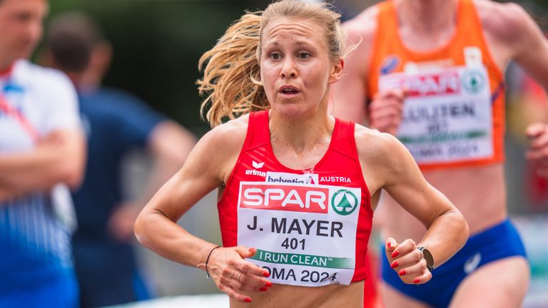 Eine Läuferin mit blonden Haaren, die ein rotes Trikot mit der Nummer 401 trägt, läuft einen Marathon. Sie konzentriert sich auf das Rennen vor sich.