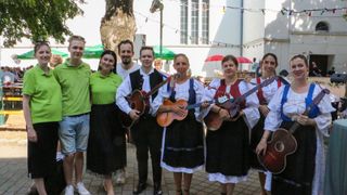Eine Gruppe von Menschen in traditioneller Kleidung, die Gitarren halten und vor einem Gebäude für ein Foto posieren.