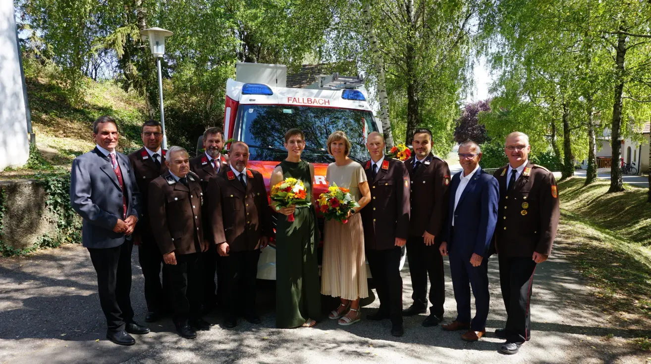 Eine Gruppe von Menschen in Uniformen und Anzügen steht vor einem Krankenwagen mit Blumen.