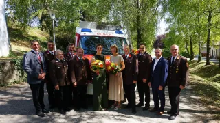 Eine Gruppe von Menschen in Uniformen und Anzügen steht vor einem Krankenwagen mit Blumen.