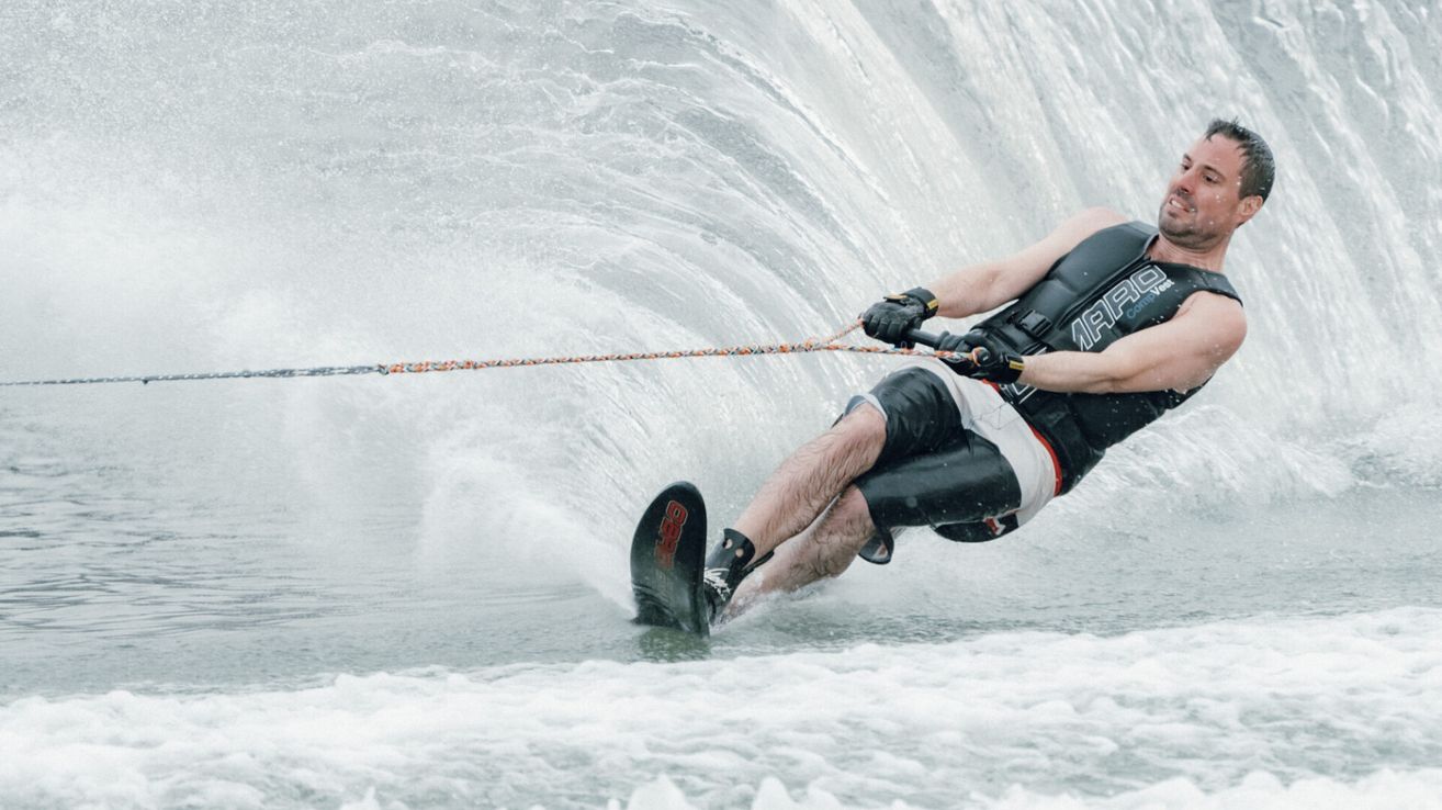 Ein Mann beim Wasserskifahren auf einem See, der an einem Seil festhält, mit Wasser, das um ihn herumspritzt.